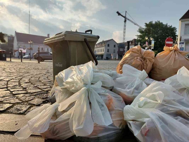 Een stapel vuilniszakken en een Interrand rolemmer op de historische Markt van Tervuren vóór de invoering van Diftar.